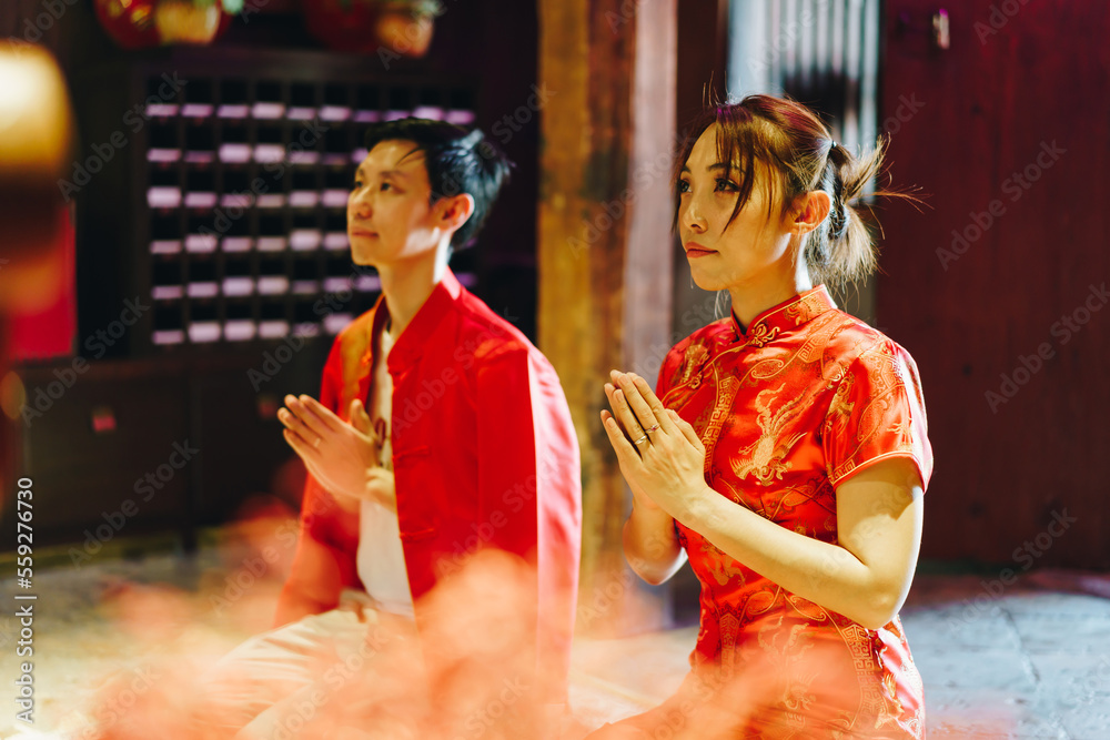 Obraz premium Happy young Asian couple in Chinese traditional dresses praying at temple
