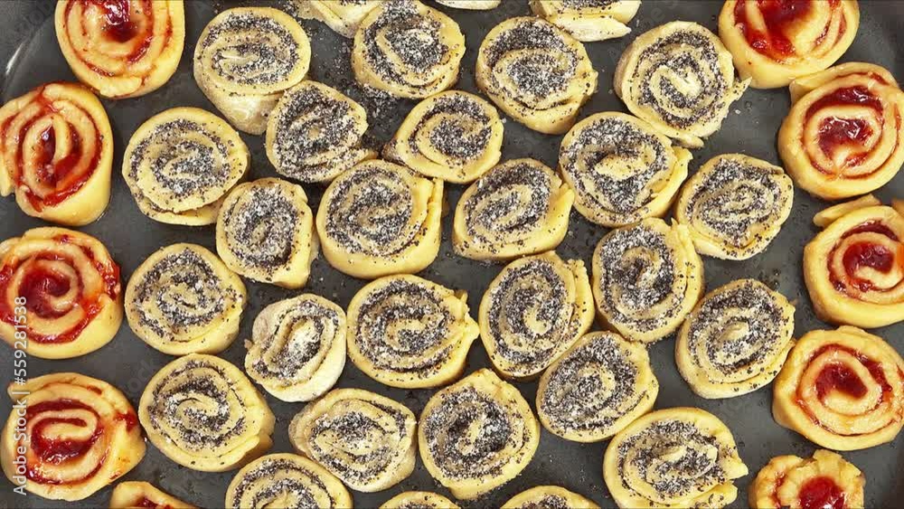 Appetizing homemade cookies in the form of rolls with poppy seeds and jam at tray ready for baking. Movement with rotation. Edible background. Close-up, flat lay, mock up, top view Appetizing homemade cookies in the form of rolls with poppy seeds and jam at tray ready for baking. Movement with rotation. Edible background. Close-up, flat lay, mock up, top view