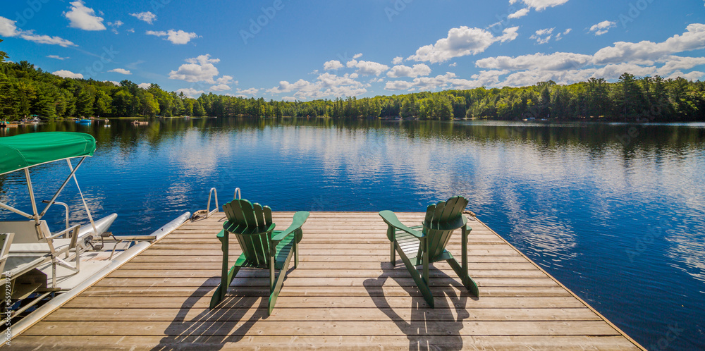 Obraz premium Two Ontario chairs sitting on a wood dock facing a calm lake.