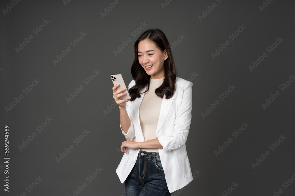 Female executive in white suit with long hair, white skin, taking photo in studio against gray background looking at cell phone His face was smiling, excited and hopeful. Female executive in white suit with long hair, white skin, taking photo in studio against gray background looking at cell phone His face was smiling, excited and hopeful.