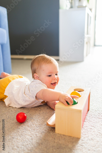 Seven month old baby playing with object permanence ball drop toy on floor