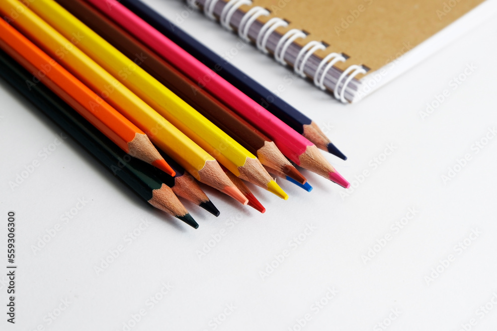 colored pencils against the background of a desk, notebook, white wall colored pencils against the background of a desk, notebook, white wall