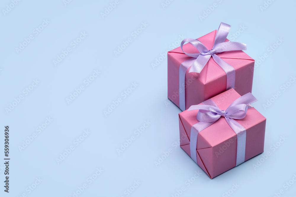 Two stylish gift boxes wrapped in pink paper, decorated with a lilac satin ribbon. Studio shot, blue background, copy space. Two stylish gift boxes wrapped in pink paper, decorated with a lilac satin ribbon. Studio shot, blue background, copy space.