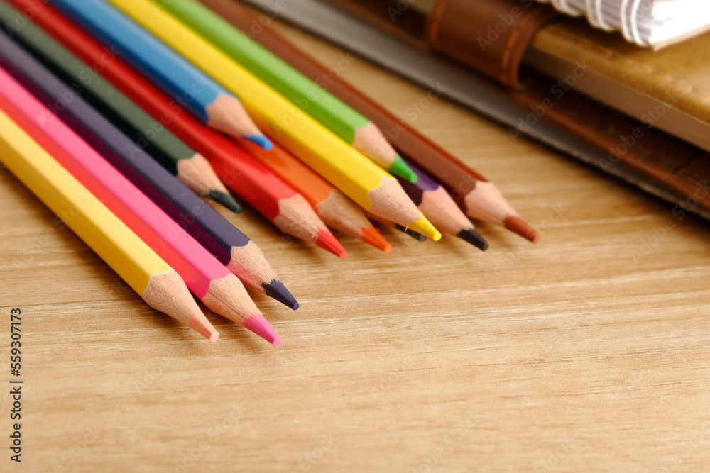 colored pencils against the background of a desk, notebook, white wall colored pencils against the background of a desk, notebook, white wall