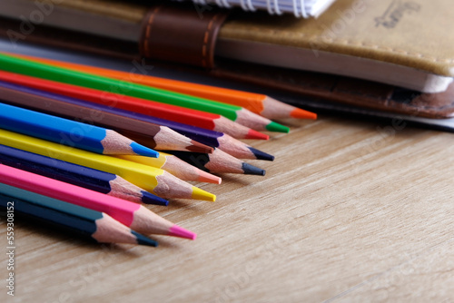 colored pencils against the background of a desk, notebook, white wall