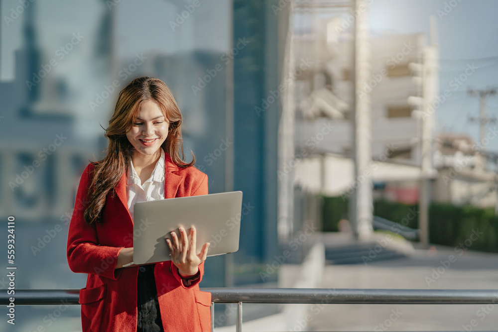 Fototapeta premium young woman using his laptop with smile while standing outdoors.