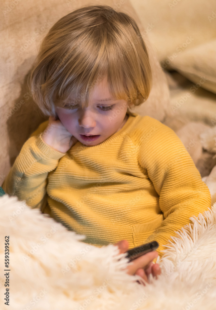 Portrait Of A Concentrated 3 Year Old Blond Boy Watching Video On Smartphone. Gesture Of Astonishment Portrait Of A Concentrated 3 Year Old Blond Boy Watching Video On Smartphone. Gesture Of Astonishment
