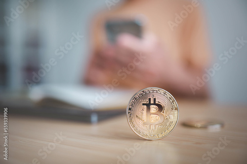 Bitcoin on the table with blured  man using mobile phone to transfer money online or financial payment and read text, digital technology concept.