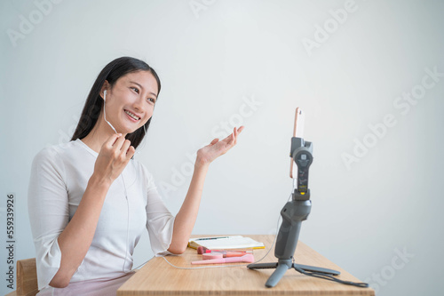 Young attractive asian woman blogger or vlogger talking on video call shooting with mobile phone and broadcast with internet subscribers. Social media influence people and Social communication.