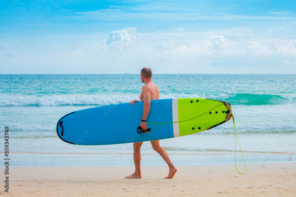 A man walks along the beach with a surfboard in his hands. Surfing on a water board. A professional surfer rides the waves. Athlete catches waves in the ocean.