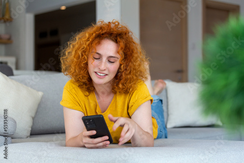Woman using mobile phone while lying on sofa. Young female is resting at home.