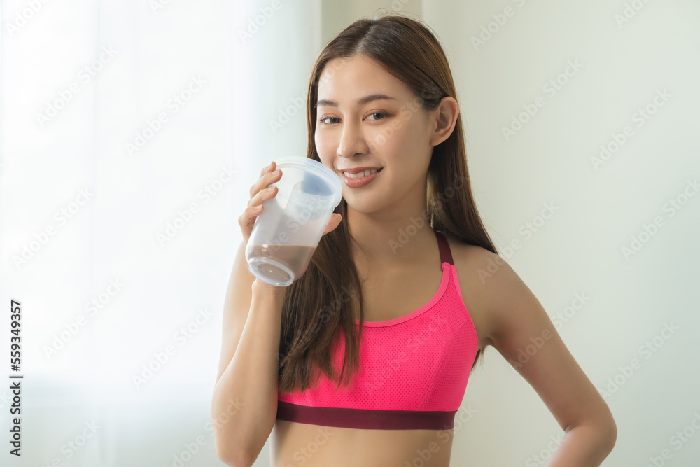 Diet meal replacement for weight loss, happy asian young woman, girl in sportswear, hand in holding protein shake bottle for drink supplement for muscle after workout at home. Healthy body care person Diet meal replacement for weight loss, happy asian young woman, girl in sportswear, hand in holding protein shake bottle for drink supplement for muscle after workout at home. Healthy body care person