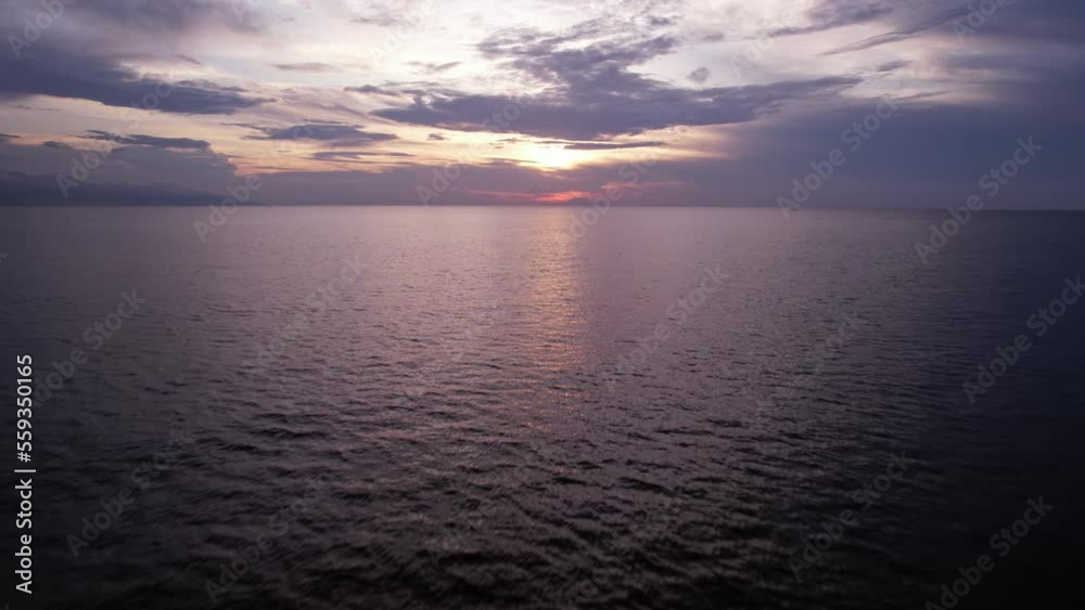 Calm ripply sea water and sunset sky, aerial camera fly back, looking to sun light shining through clouds at horizon line. Wide angle shot, hypnotizing ocean surface in motion Calm ripply sea water and sunset sky, aerial camera fly back, looking to sun light shining through clouds at horizon line. Wide angle shot, hypnotizing ocean surface in motion