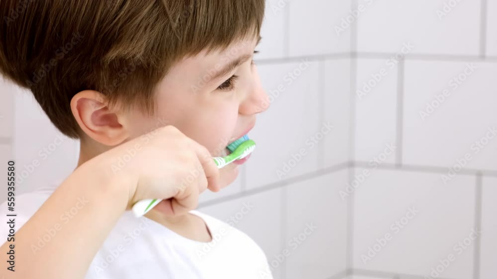 A cute little child brushes teeth. Green toothbrush. Daily morning hygiene procedures in a white bathroom. Portrait of beautiful caucasian 6 year old boy. Teeth brushing concept. Copy space. Close-up. A cute little child brushes teeth. Green toothbrush. Daily morning hygiene procedures in a white bathroom. Portrait of beautiful caucasian 6 year old boy. Teeth brushing concept. Copy space. Close-up.