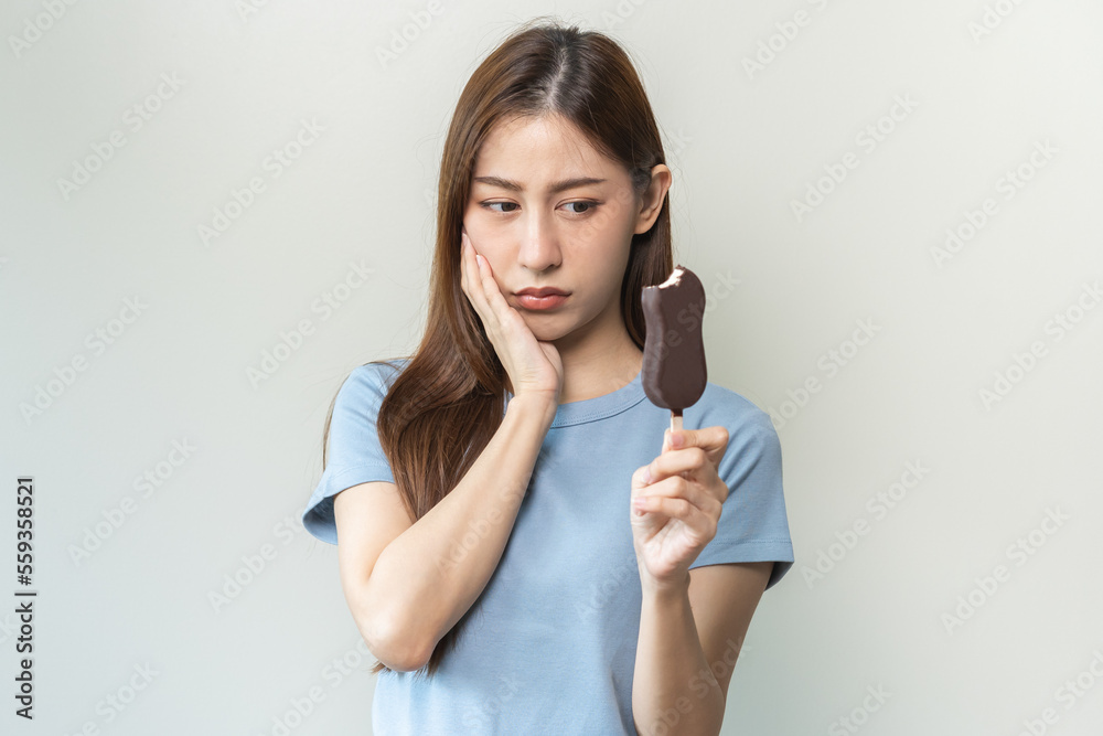 Face expression suffering from sensitive teeth and cold, asian young woman, girl feeling hurt, pain eating ice cream, lolly. Toothache molar tooth at home, dental problem isolated on white background. Face expression suffering from sensitive teeth and cold, asian young woman, girl feeling hurt, pain eating ice cream, lolly. Toothache molar tooth at home, dental problem isolated on white background.