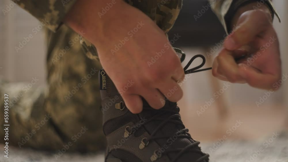 Close-up hands of military man tying laces on boots, ready for training in army