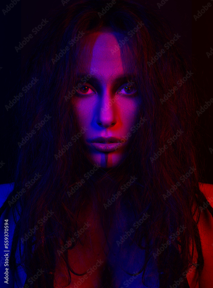 Beautiful woman studio portrait illuminated in red and purple color. Model with messy dreadlocks hair and make-up looking to camera with seductive look. Futuristic looking style. Toned image