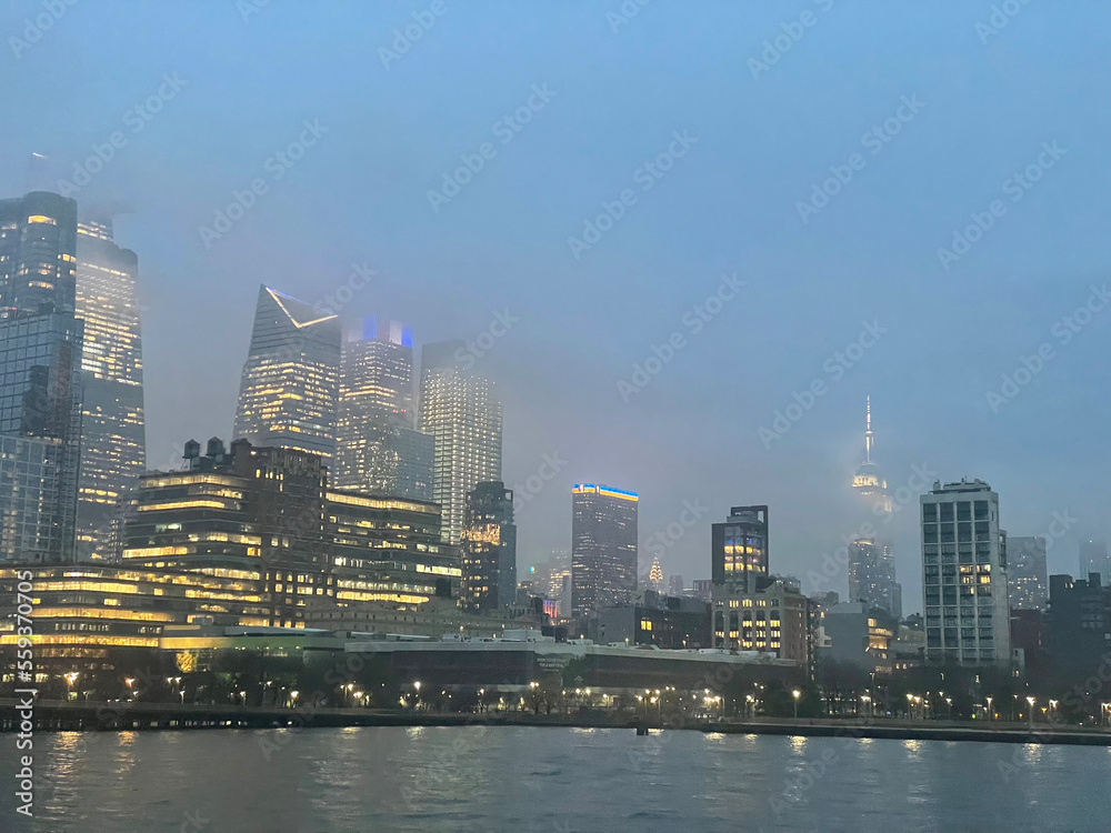 New Financial District skyscrapers in Chelsea and Hell's Kitchen from the Hudson River with the Empire State Building in the background on the right on a foggy evening.