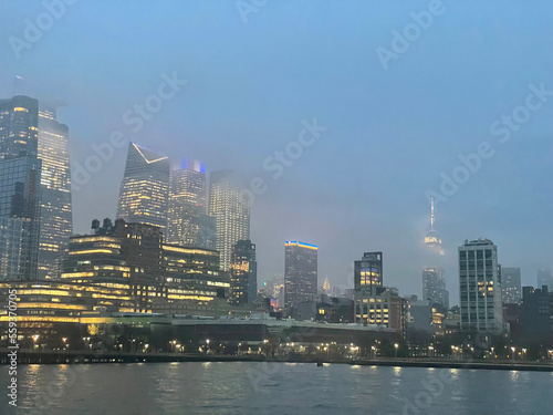 New Financial District skyscrapers in Chelsea and Hell's Kitchen from the Hudson River with the Empire State Building in the background on the right on a foggy evening.