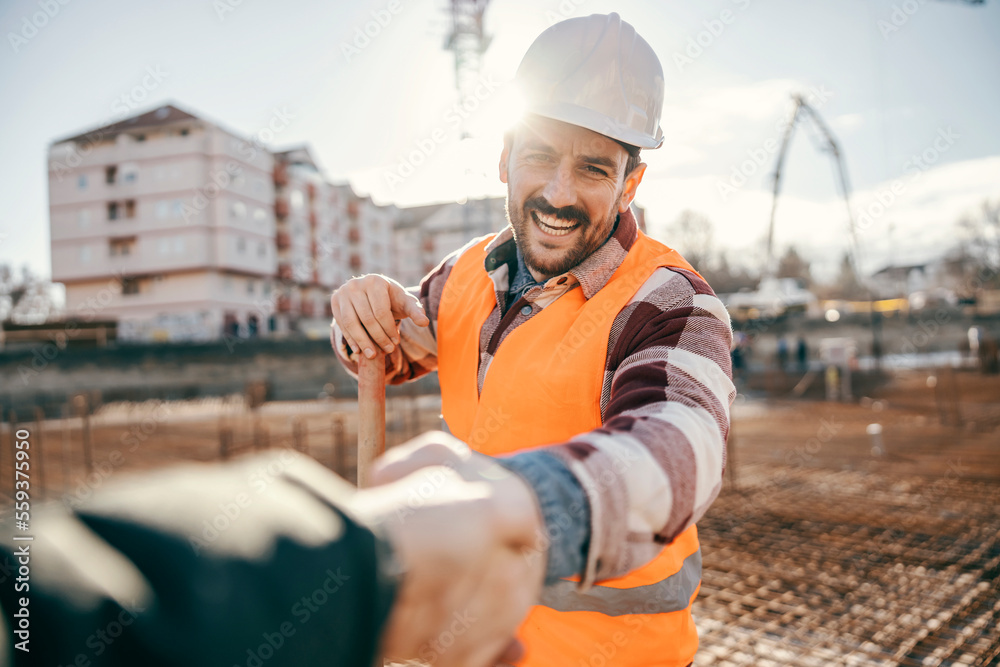 A happy site worker is shaking hands with site manager while standing at site.