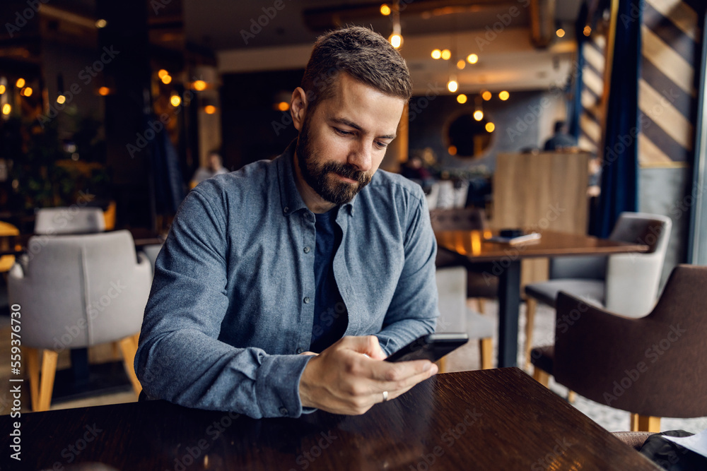 A man sits in a coffee shop and uses his phone. A man sits in a coffee shop and uses his phone.