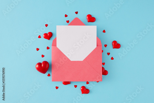 St Valentines Day concept. Flat lay composition made of paper envelope with letter and heart shaped red sprinkles on blue background. Minimal Valentines card idea.
