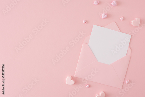 Valentines Day concept. Flat lay photo of envelope with letter and pink heart shaped baubles on pastel pink background with copy space. Women's day celebration idea. © Goncharuk film