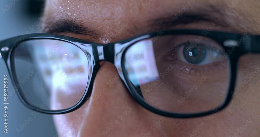 Close up of businessman in eyeglasses working at a computer in the evening, the image from the monitor is reflected on his glasses. Businessman glasses reflect computer monitor while working, macro.