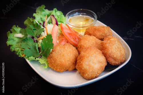 Thai traditional deep fry shrimp patty in a plate on table with sweet plum sauce with isolated black background. It made with mince fresh shrimp cover with breadcrumbs 