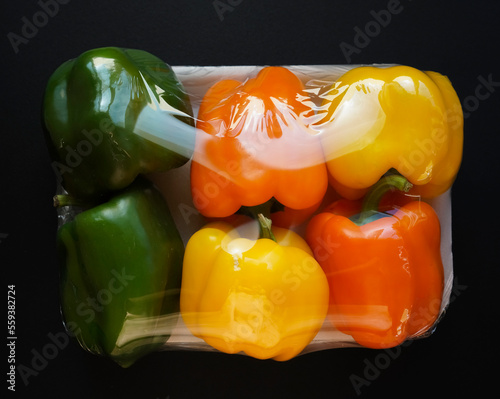 Assorted bell peppers in plastic wrap. sweet colorful paprikas are wrapped in plastic foil, packed. isolated on black  background.