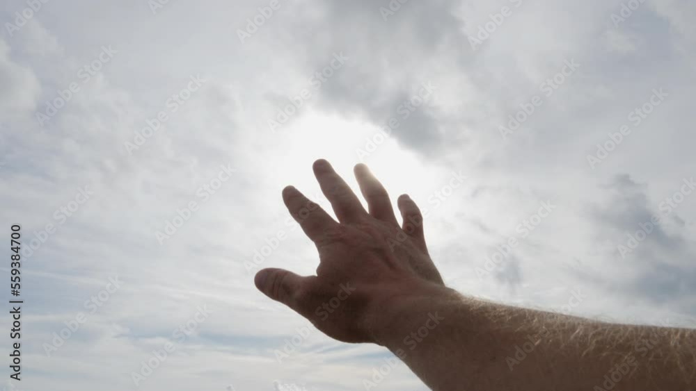 Man's hand palm reaching toward the sunshine into a cloudy sky Man's hand palm reaching toward the sunshine into a cloudy sky