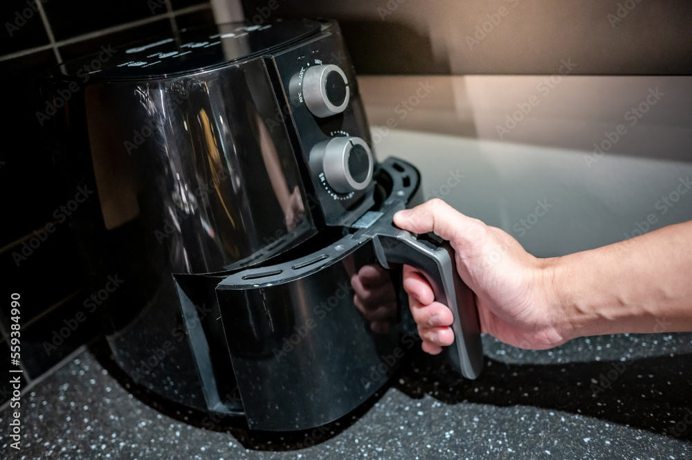 Male hand holding an electric air fryer handle in the kitchen. Home appliance for healthy cooking lifestyle. Male hand holding an electric air fryer handle in the kitchen. Home appliance for healthy cooking lifestyle.