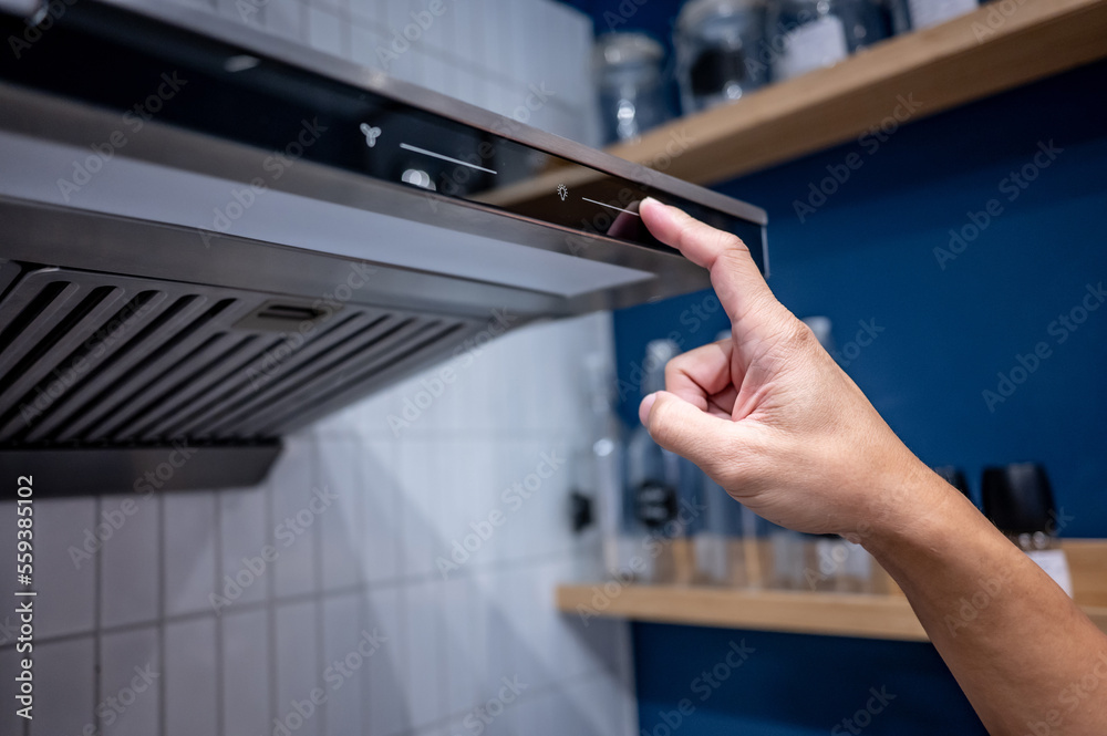 Male hand turn on extractor fan and light of cooker hood in the kitchen. Modern home appliance for cooking lifestyle.