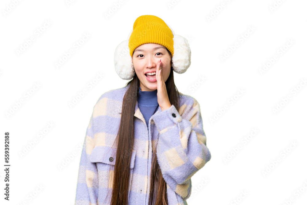 Young Asian woman wearing winter muffs over isolated chroma key background shouting with mouth wide open