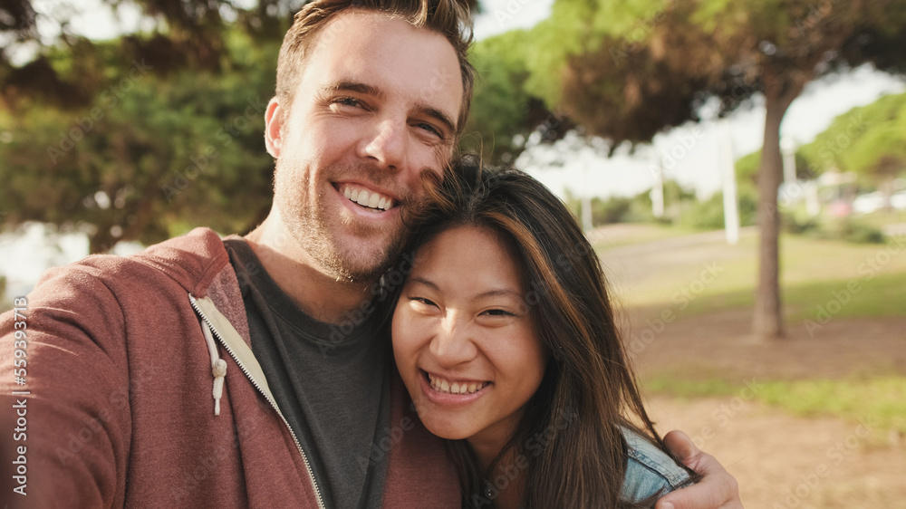 Close up, laughing couple hugging each other while standing in the park. looking at camera Close up, laughing couple hugging each other while standing in the park. looking at camera