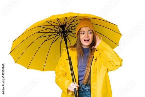 Young pretty woman with rainproof coat and umbrella over isolated chroma key background listening to something by putting hand on the ear