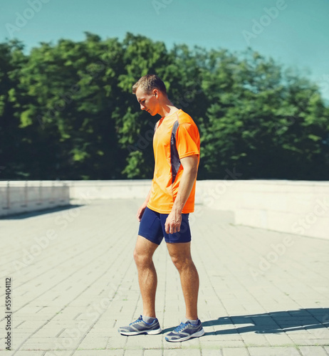Sport and healthy lifestyle concept - sporty fitness runner man standing in the city park, ready for working or resting after run training outdoors