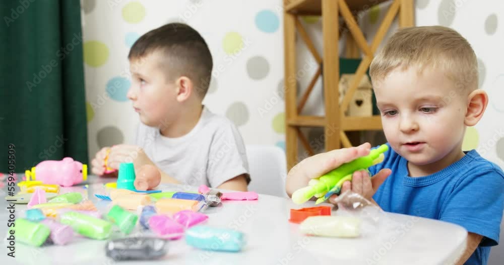 Cute children sitting at the table and plays with playdough
