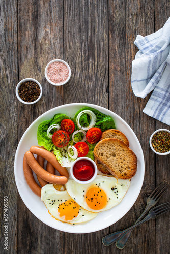 Breakfast - sunny side up egg, boiled sausages and vegetables served on wooden table 