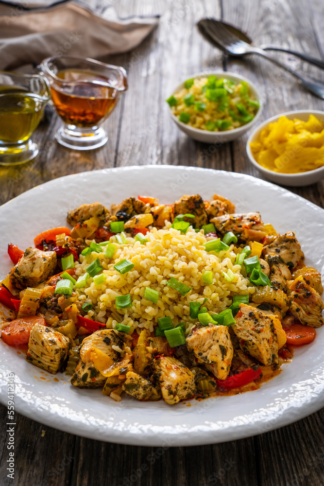 Fried chicken nuggets, bulgur groats, carrots and red pepper on wooden background
