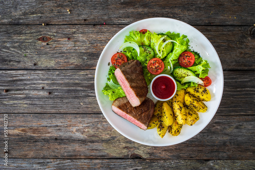 Fried beef sirloin with potatoes and vegetables on wooden table 