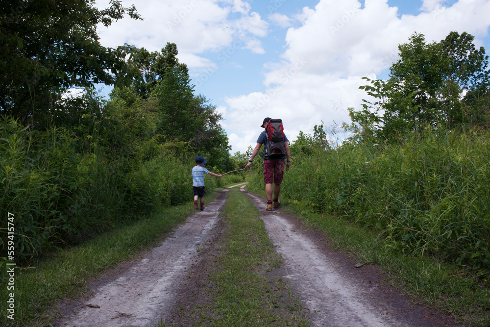 Rear view of father and son playing with stick while walking on tire tracks Rear view of father and son playing with stick while walking on tire tracks