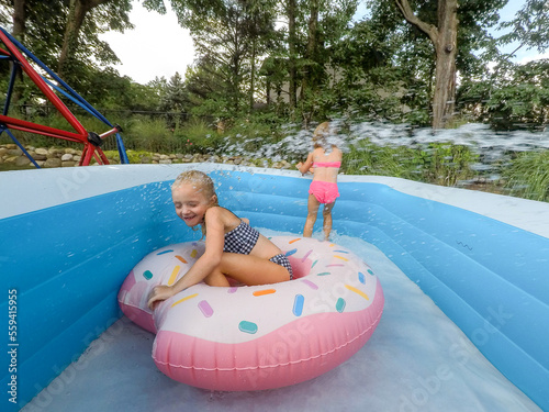girl playing in raft with water being sprayed on her from garden hose