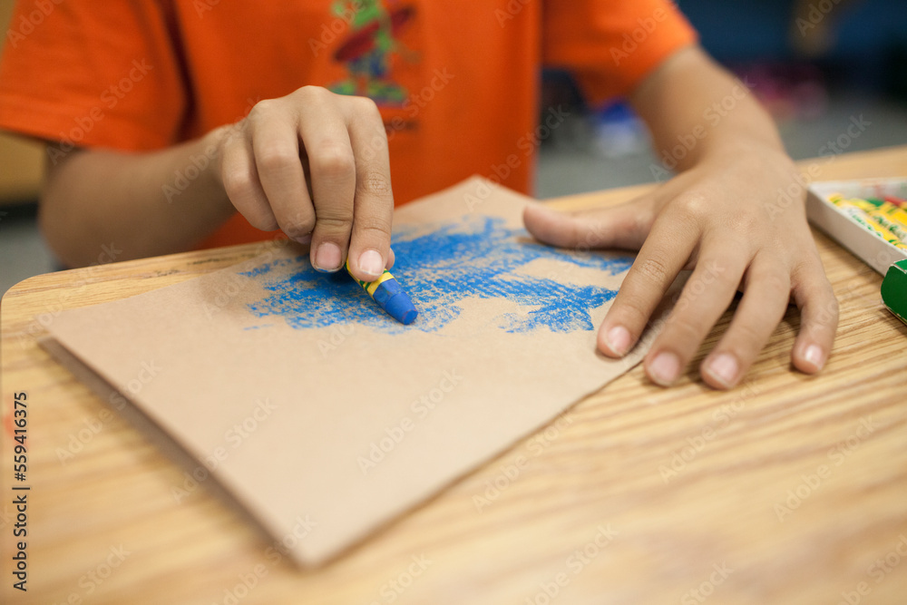 A young boy colors using a blue crayon. A young boy colors using a blue crayon.