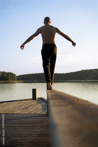 A man balances barefoot on a rail of a wooden pier at the shores at one of the thousands of lakes in the Saimaa region of Finlan photo