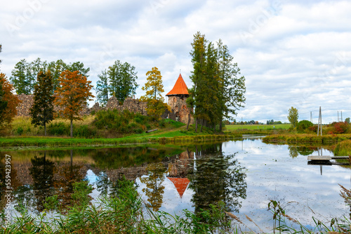 colorful autumn landscape with ruins of an old castle, restored roof of the castle tower, colorful reflections on the surface of a calm lake photo