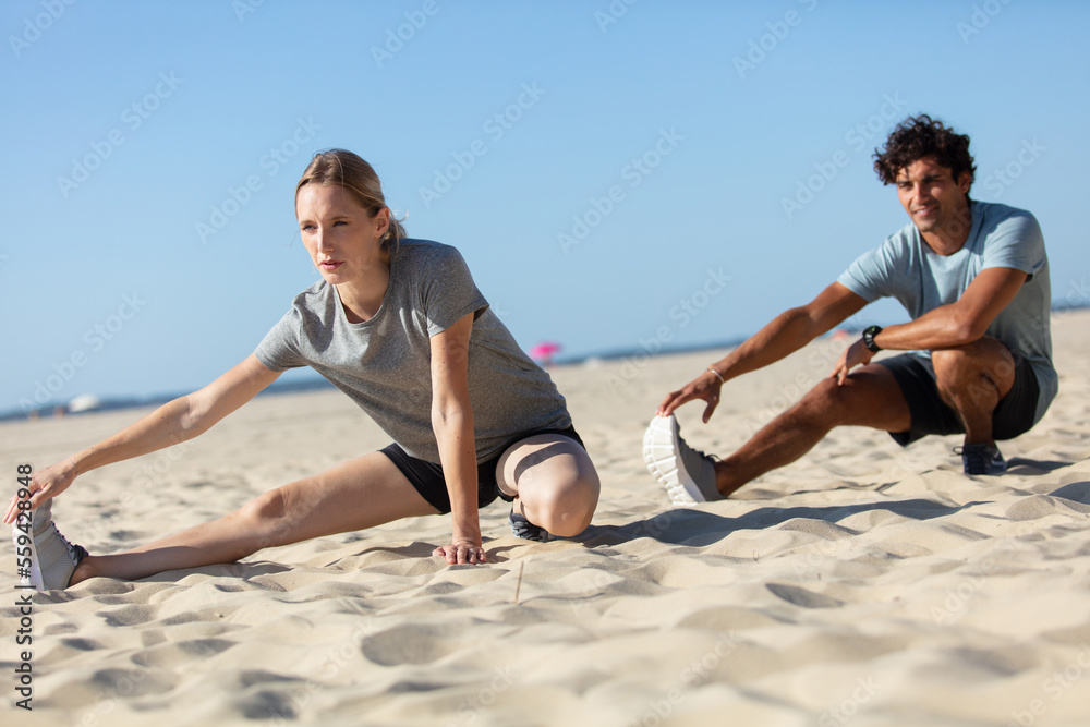 young couple of man and woman stretching on ocean beach young couple of man and woman stretching on ocean beach