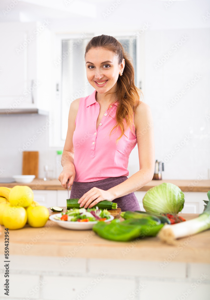 Portrait of woman standing at kitchen table at home, slicing vegetables, cooking salad