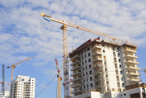 A construction site, a white building and a tall construction crane. Developers industry. Buying a home, mortgage. Modern residential buildings. Space for text, blue sky, summer