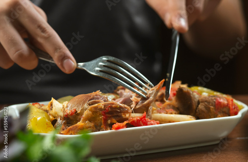 left-handed man eats lamb stew on the bone with vegetables.Khashlama is popular Armenian dish, which is prepared from beef with vegetables. Khashlama in the plate. caucasian food